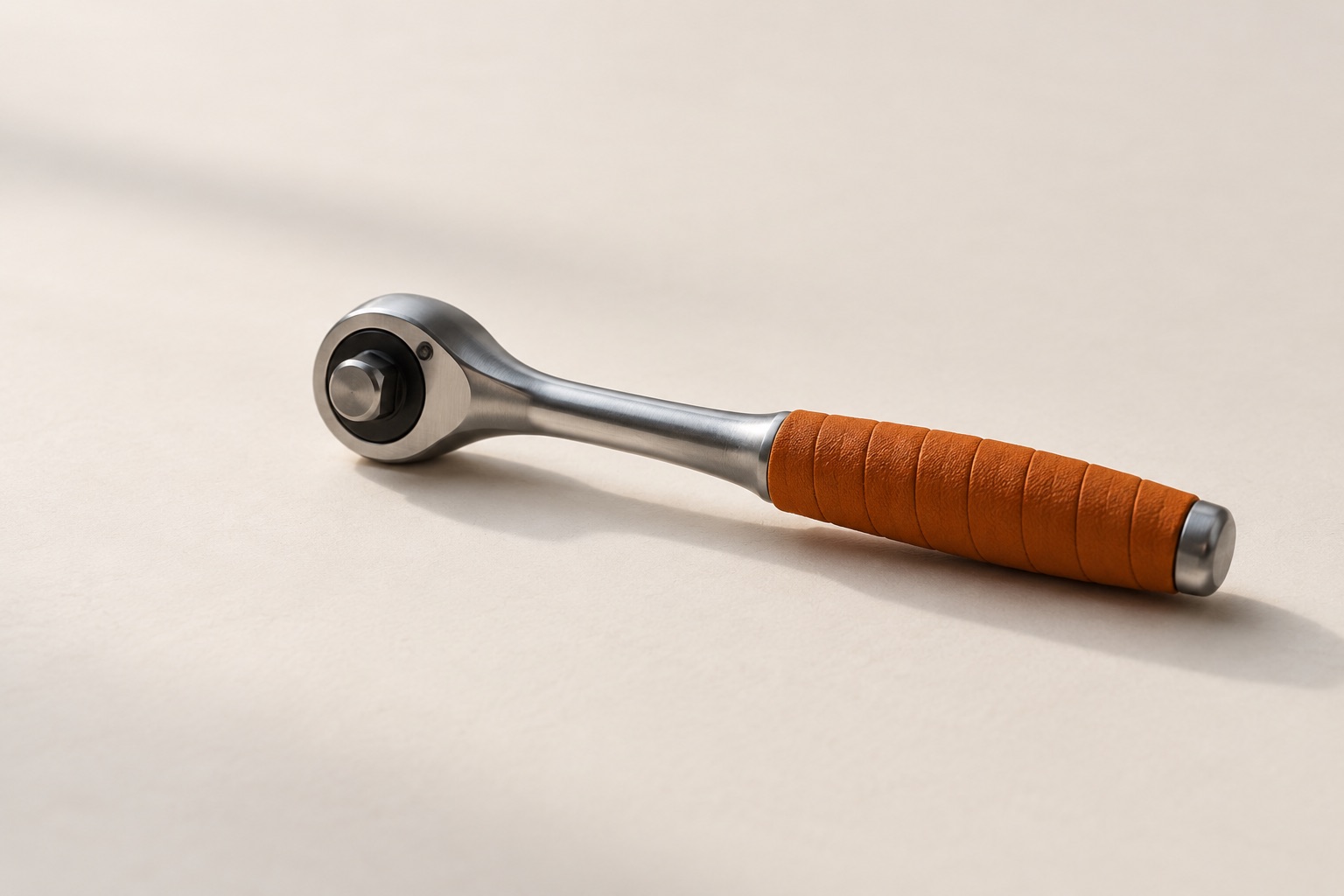 A steel ratchet wrench lying on warm off-white paper, its handle wrapped in burnt-orange grip tape.