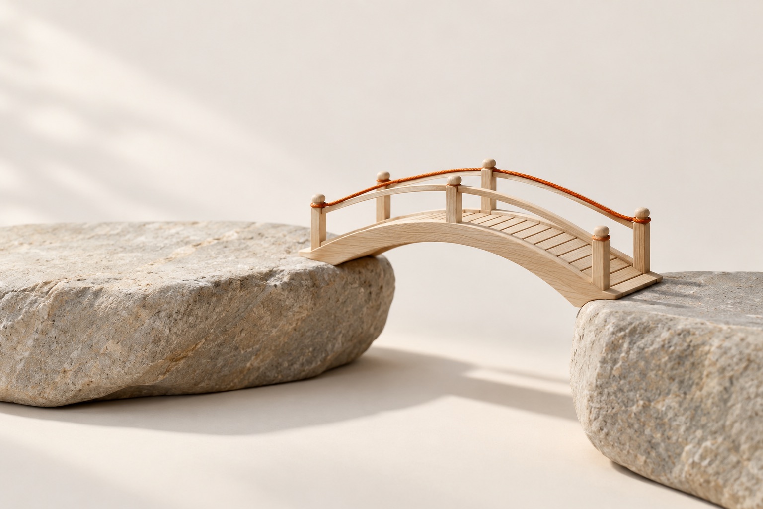 A small arched wooden footbridge spanning a gap between two stone blocks, with an orange thread along its handrail.